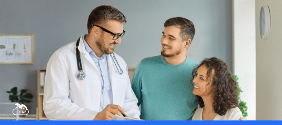 Médico de óculos e jaleco explicando algo para um casal sorridente e engajado em seu consultório, ilustrando o atendimento humanizado e a satisfação do paciente com a comunicação e o cuidado recebido.