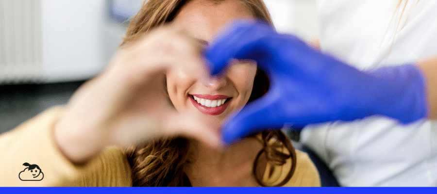 Paciente sorridente formando um coração com as mãos junto a um profissional de saúde, simbolizando cuidado e confiança no atendimento.