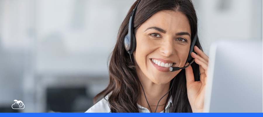 Close-up de uma mulher morena sorridente, usando um headset de atendimento e olhando para a câmera, simbolizando o atendimento humano por trás da tecnologia e a importância de um chatbot humanizado com suporte de pessoas.