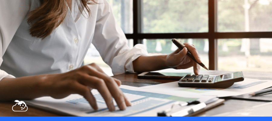 Uma profissional (médica ou contadora) sentada à mesa de escritório utilizando uma calculadora e analisando documentos financeiros. A imagem ilustra o planejamento do imposto de renda para médicos, com foco nas mãos da pessoa manuseando papéis e uma caneta em um ambiente iluminado.