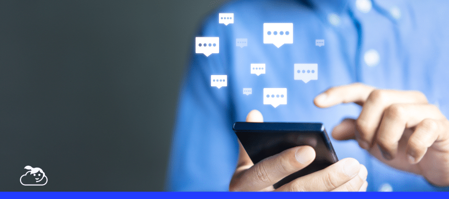 Homem de camisa azul usando um smartphone, com ícones de balões de conversa flutuando acima, simbolizando a comunicação e o uso de um chatbot para clínicas ou atendimento automatizado.