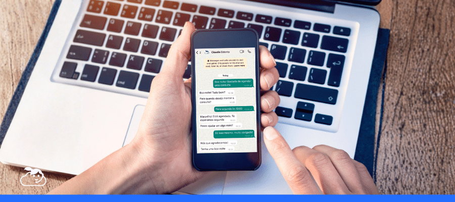 Mãos segurando um smartphone com uma conversa de chatbot no WhatsApp aberta (da Clínica Corintho), mostrando o agendamento de uma consulta e a interação através de texto, demonstrando o uso da API WhatsApp Business para automação de conversas.