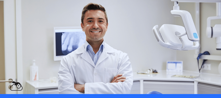 Dentista sorrindo em consultório odontológico moderno, com equipamento clínico e radiografia ao fundo, representando o uso de inteligência artificial na odontologia para apoio ao diagnóstico, planejamento de tratamentos e inovação no atendimento ao paciente.